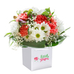 A radiant bouquet overflowing with the heartbeat of Seven Sisters, this arrangement is artfully presented in a crisp, square white bag poised for delivery. Soft coral and vibrant red carnations, alive with exuberant ruffles, mingle with playful white daisies topped by bright yellow-green eyes, conjuring the easy optimism of a sunny afternoon at Downhills Park. Wispy baby's breath, scattered delicately throughout, dances like confetti in a local celebration, while hints of unopened, purple-blushed buds add a hushed anticipation that speaks of new joys on the horizon. Surrounding the blooms, deep green glossy leaves form a foundation that feels both grounded and generous, echoing the lushness of tree-lined residential streets near Seven Sisters station. The bag's gently arched ribbon handles make this bouquet easy to carry-its balanced proportions an invitation to pause and delight. Lit in a way that flatters every nuance, each element glows with freshness and intent, ideal for marking a birthday, an anniversary, or brightening a room in nearby Harringay. Perfectly structured without sacrificing warmth, this bouquet channels the charm of Seven Sisters through every petal and leaf, offering the sincere joy and artistry of a passionate local florist.